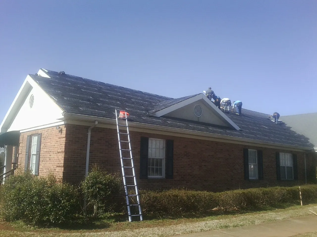 Crew tearing shingles off a brick ranch roof with a ladder set — Metal Roof Repair work by our crew in Oilville