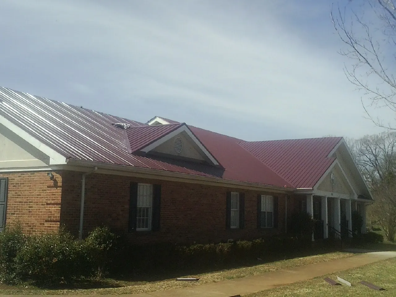 Red metal roof with gabled entries on a long brick building, from a Hail Damage Roof Repair job in Oilville