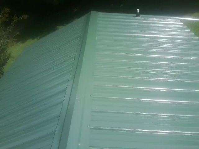 New green metal panels meeting at the ridge of a roof — Flat Roof Repair work by our crew in Oilville