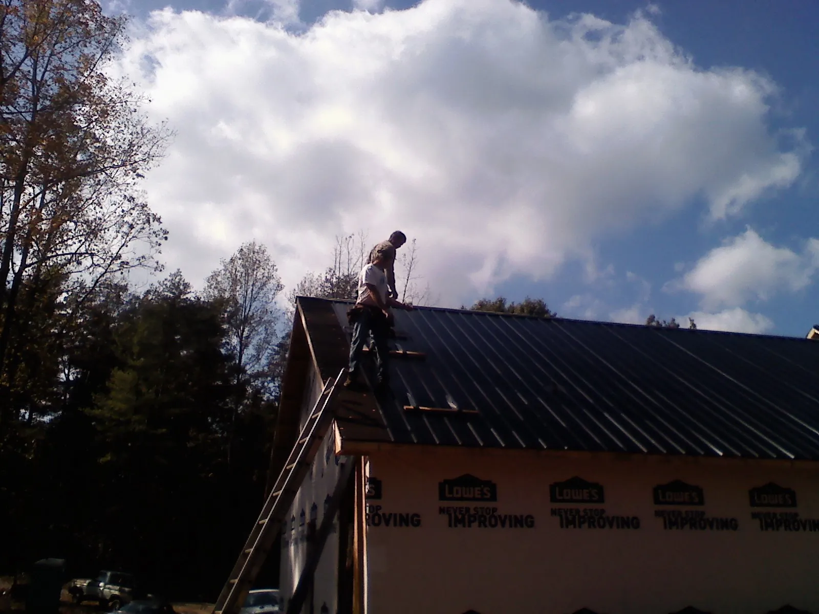 Roofer fastening dark metal panels high against a cloudy sky, from a Roof Inspection job in Oilville