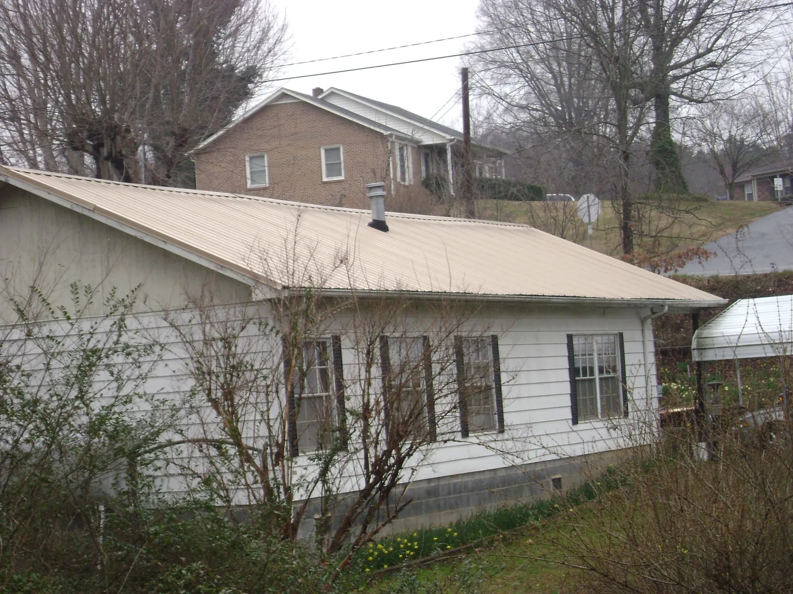 Tan metal roof on a white sided house set into a hillside — Commercial Roofing by Roofing Brothers in Oilville